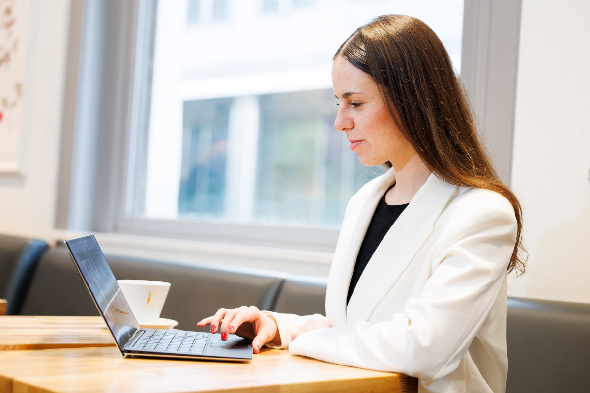 Foto: Eine Frau sitzt auf einer Bank und benutzt ein Notebook dass auf einem Tisch steht.