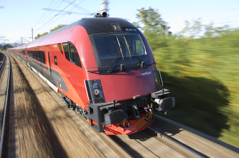 Ein Railjet-Zug der ÖBB ist von vorne, während der Fahrt, zu sehen. Der Zug hat die Farben rot und schwarz.