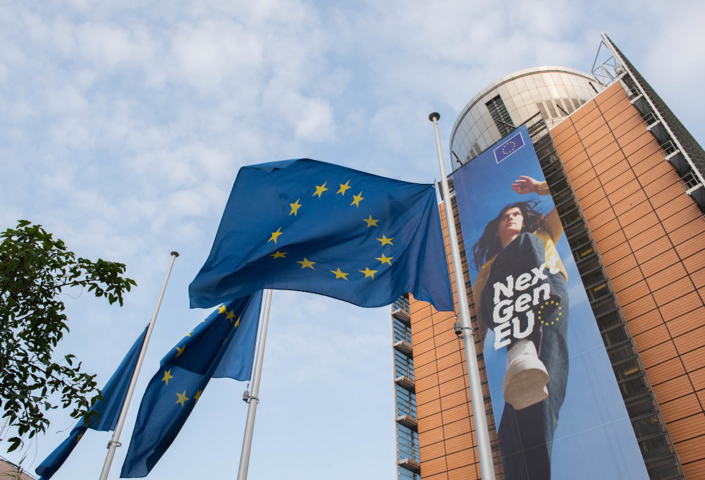Europaflaggen wehen vor einem EU-Gebäude, zu sehen ist auf dem Gebäude ein großes Plakat mit Aufschrift "NextGenEU"