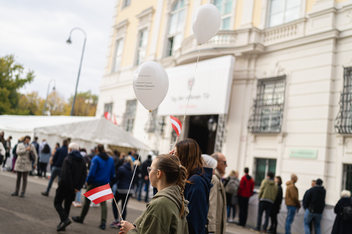 Zwei Personen mit der Österreichischen Nationalflagge und einem Luftbalon vor dem Bundeskanzleramt